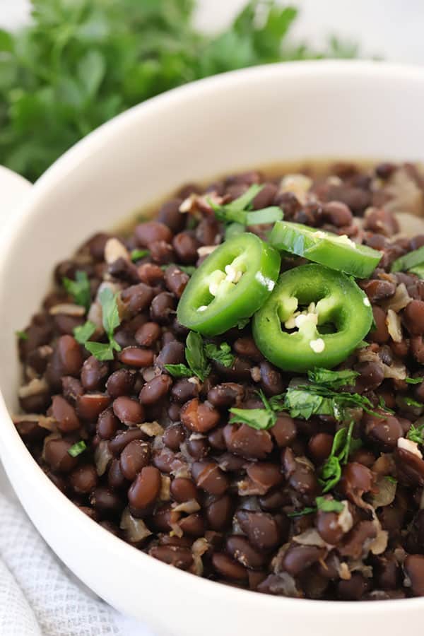 Chipotle Black beans in a serving dish topped with sliced jalapenos and fresh cilantro. black beans chipotle.