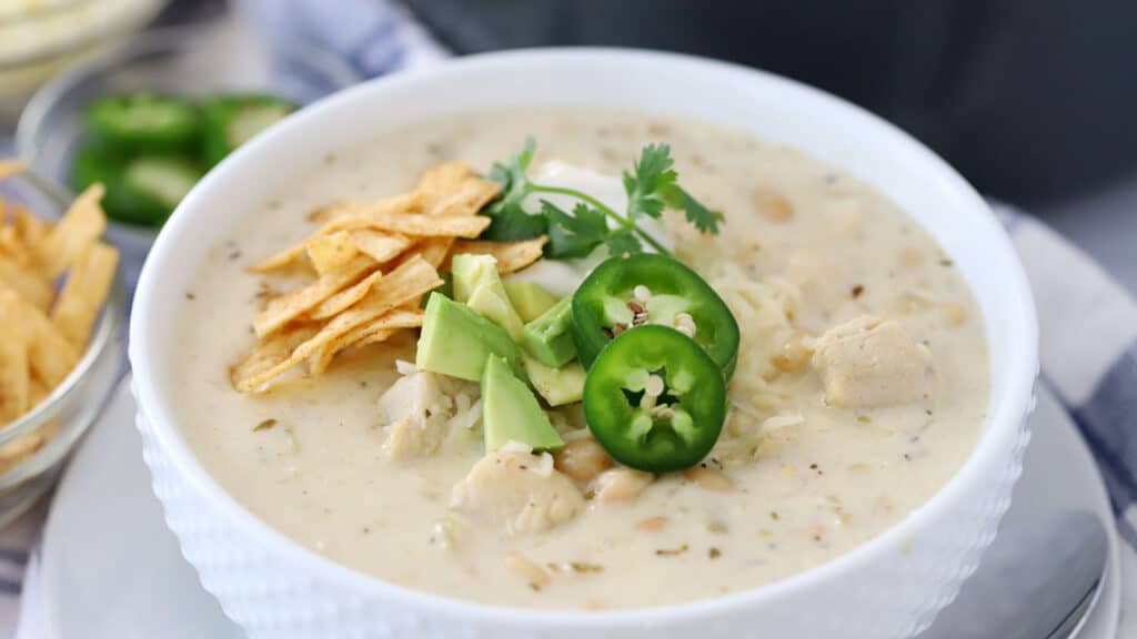 white chicken chili recipe in a small bowl with cheddar cheese, jalapeno and avocado. 
