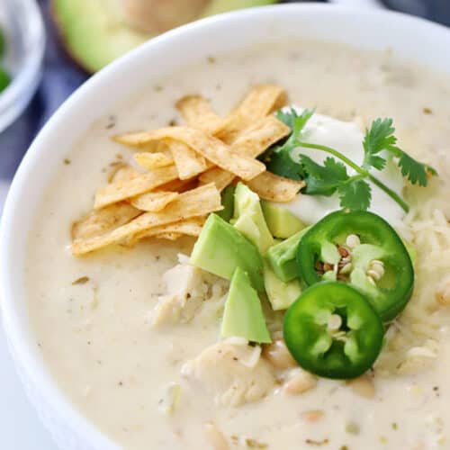 White chicken chili in a bowl, garnished with tortilla strips, avocado and sliced jalapenos.