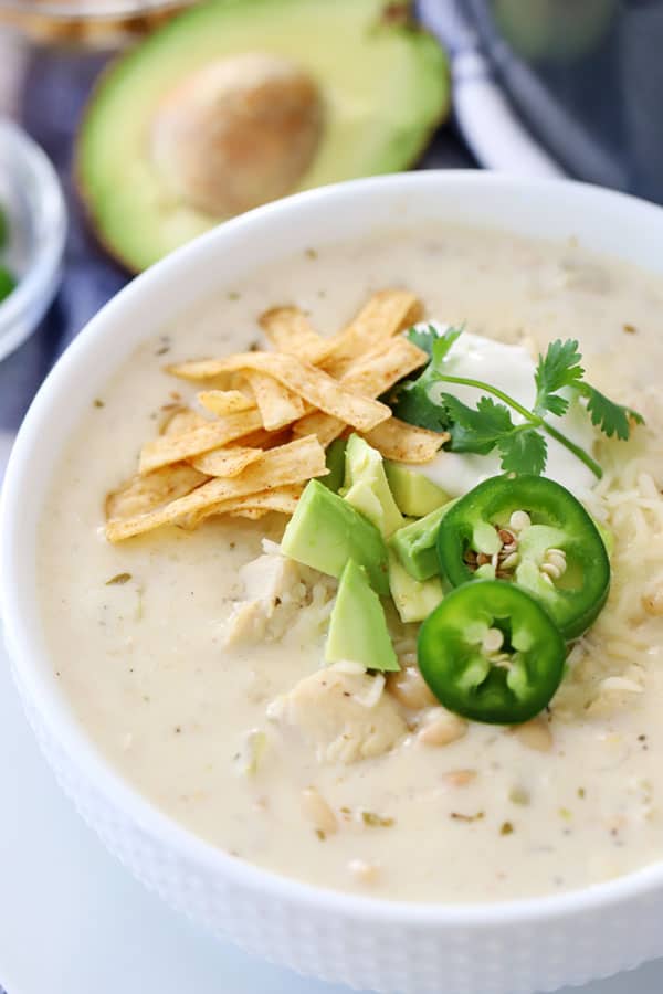 A bowl of white chicken chili garnished with fried tortilla strips, jalapenos and avocado.