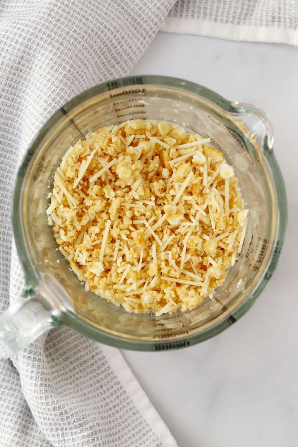Ritz crackers and grated Parmesan cheese in a glass measuring cup.