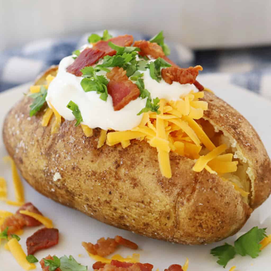 A baked potato split open and filled with shredded cheese, sour cream, bacon, and parsley. Valentines day dinner ideas. 