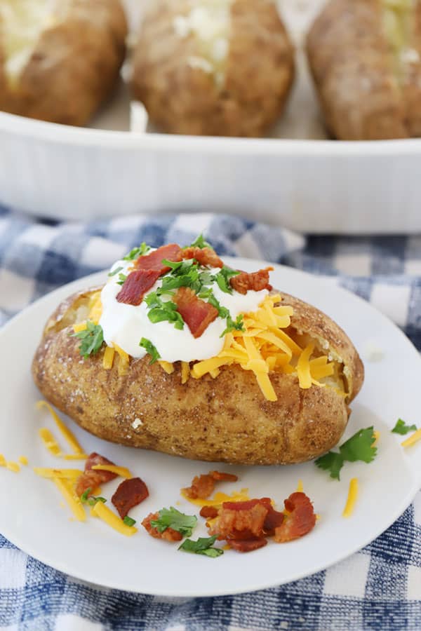 perfect baked potato made in the oven with toppings like sour cream, chives, shredded cheese and bacon bits.