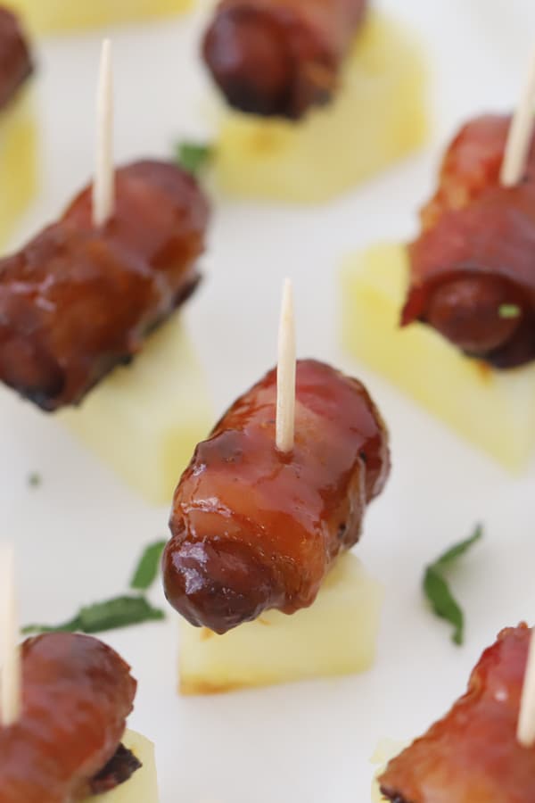 Bacon wrapped smokies with a toothpick resting on a piece of pineapple.