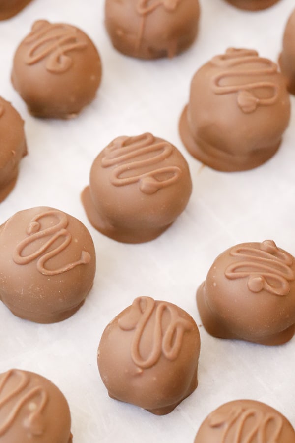 Chocolate covered coconut balls candy on a baking sheet lined with parchment paper.