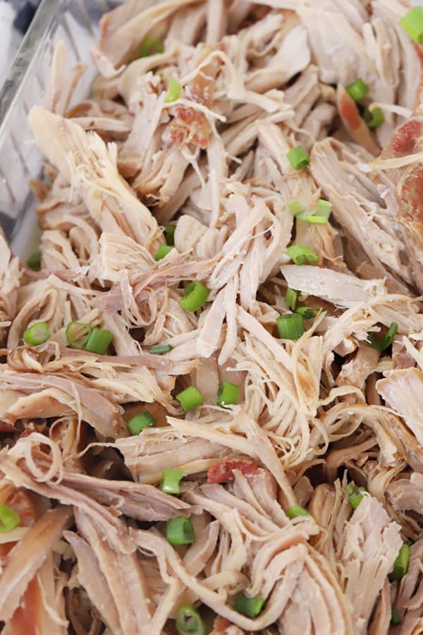 Kalua pork in a baking pan topped with chopped scallions.