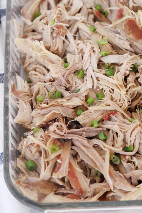 Shredded Kalua Pork in a baking dish topped with scallions.
