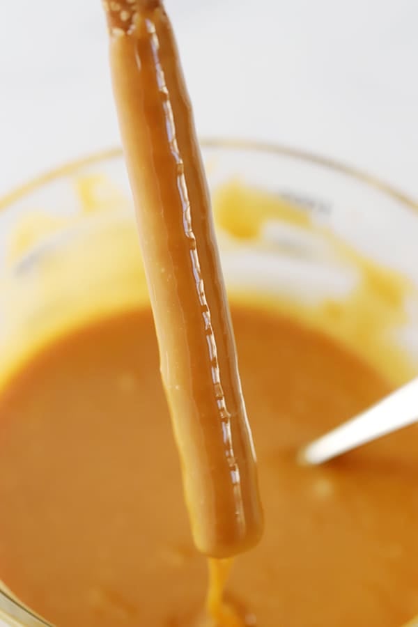 pretzel rod being dipped in a large bowl of caramel sauce
