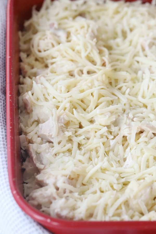 Unbaked casserole with cheese, chicken and pasta in a red baking dish.