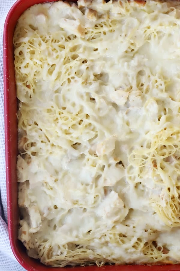 Baked spaghetti with cheese and chicken in a red baking dish.