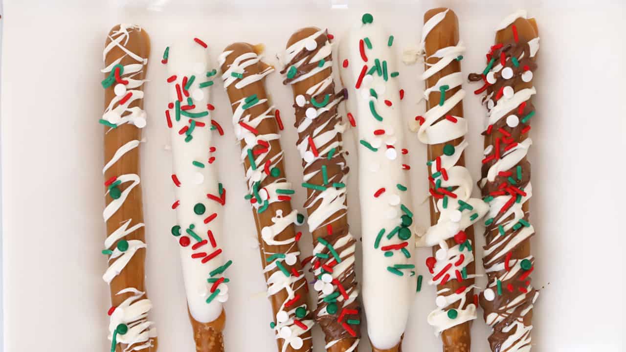 Caramel and chocolate covered pretzel rods decorated with red and green sprinkles.