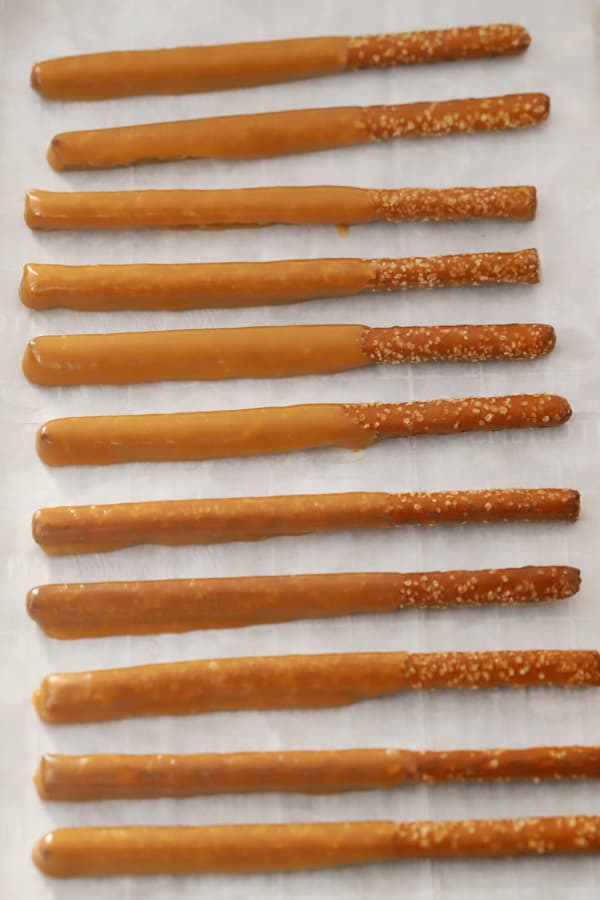 Pretzel rods dipped in caramel on a parchment paper lined sheet tray.