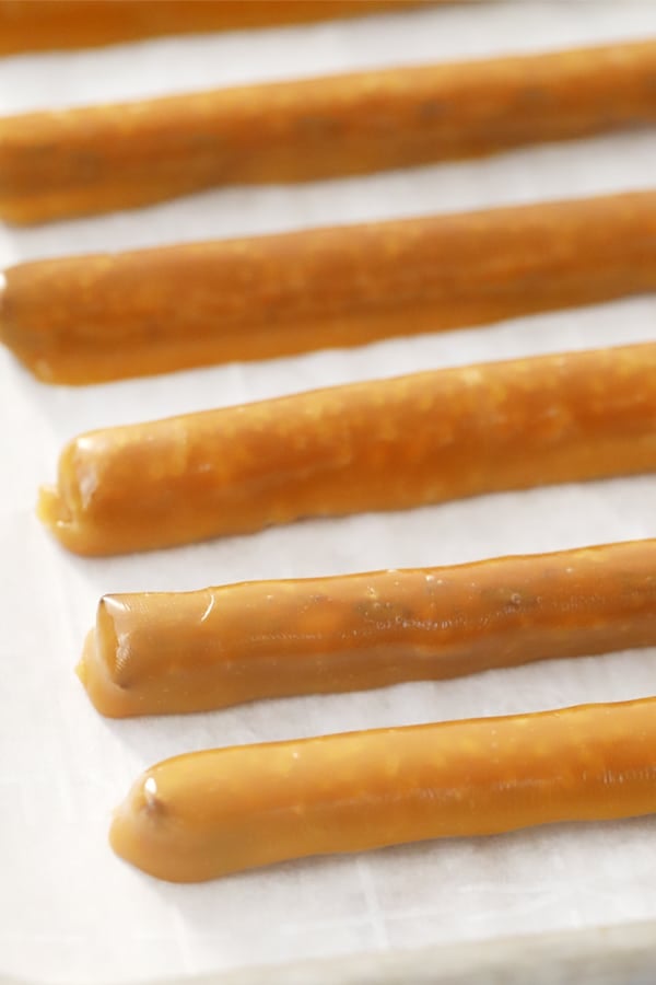 Caramel covered pretzel rods lined up on a sheet tray.