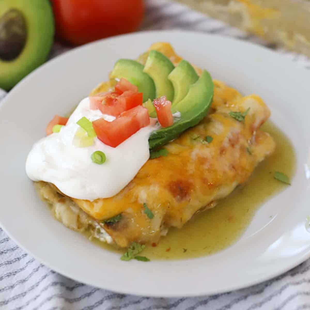green chile chicken enchilada topped with sour cream, avocados,and tomatoes
