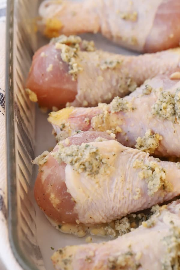Raw chicken drumsticks in a baking dish topped with garlic butter and ready to bake.
