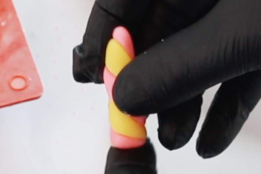 Gloved hands using starburst to make a unicorn horn for a hot chocolate bomb recipe.