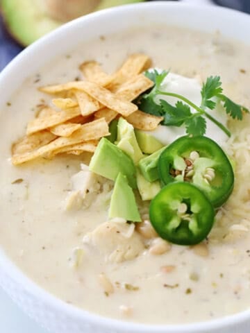 easy White chicken chili recipe in a bowl, garnished with tortilla strips, avocado and sliced jalapenos.