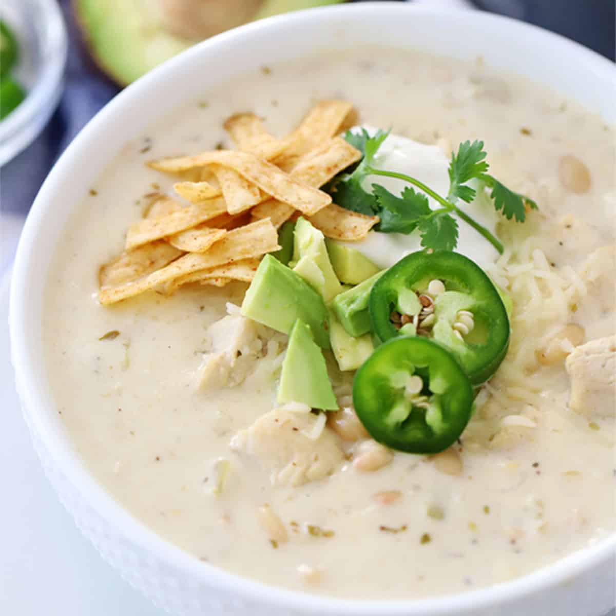 easy White chicken chili recipe in a bowl, garnished with tortilla strips, avocado and sliced jalapenos. white chicken chili easy.