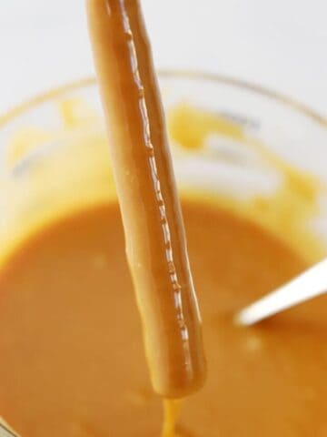 pretzel rod being dipped in a large bowl of caramel sauce