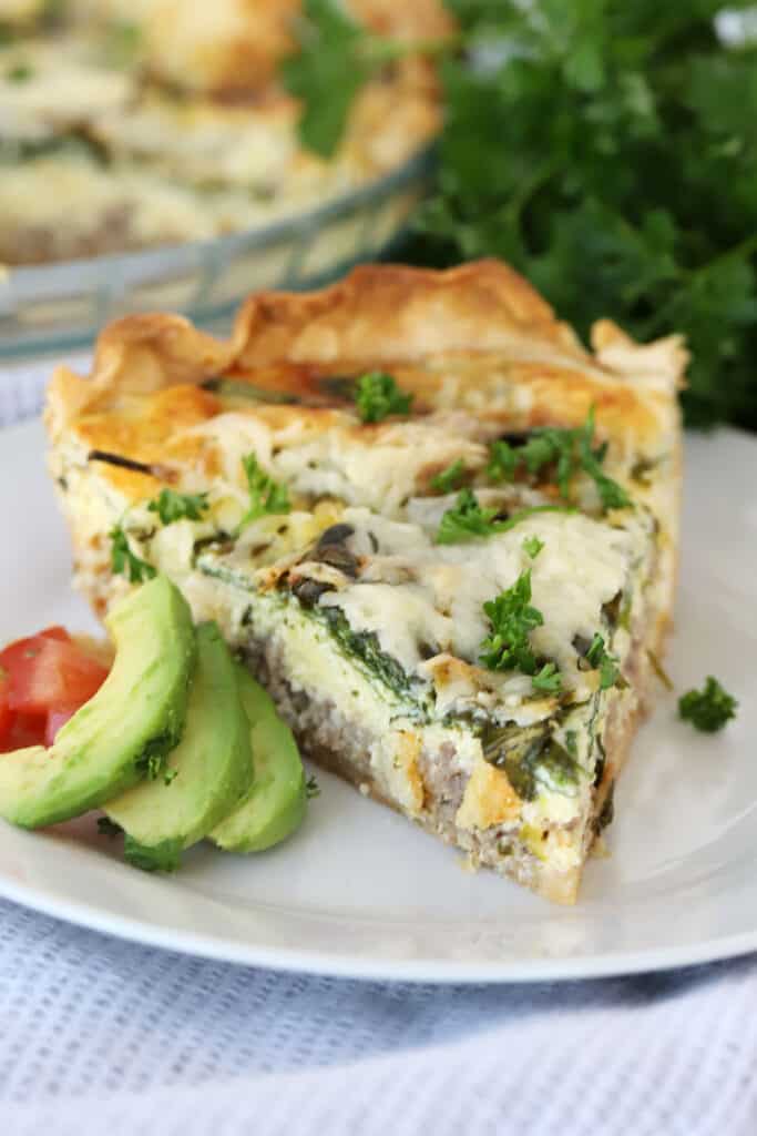 sausage and spinach quiche recipe on a plate with sliced avocado. The best Sausage and cheese quiche.
