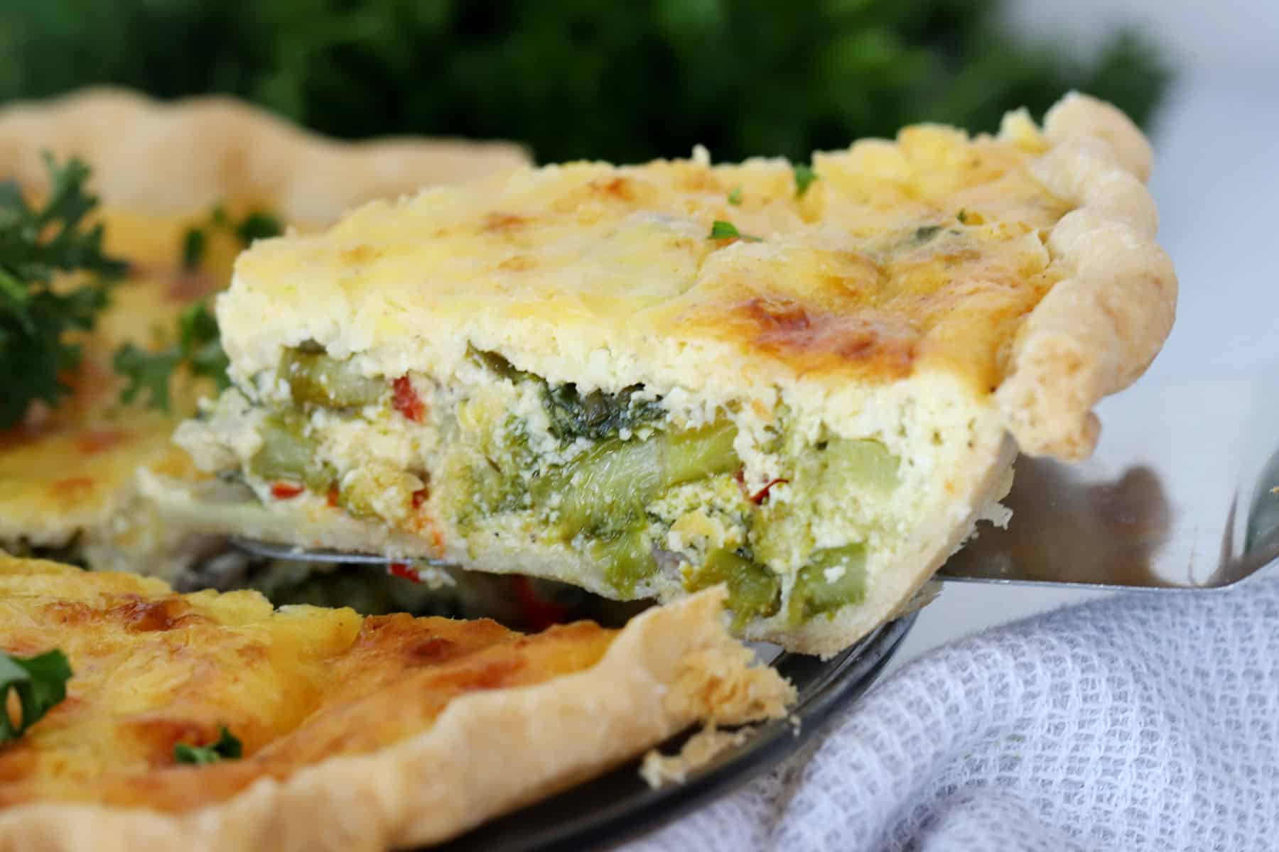 A slice of vegetable quiche being removed from a pie dish.
