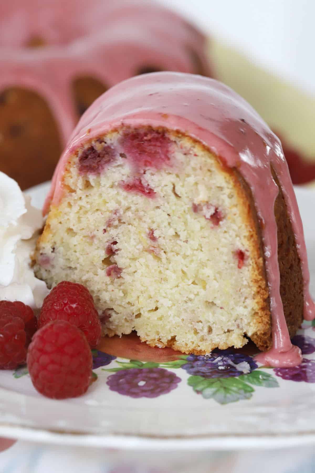 A close up of a slice of raspberry lemon bundt cake topped with raspberry glaze and garnished with fresh raspberries.