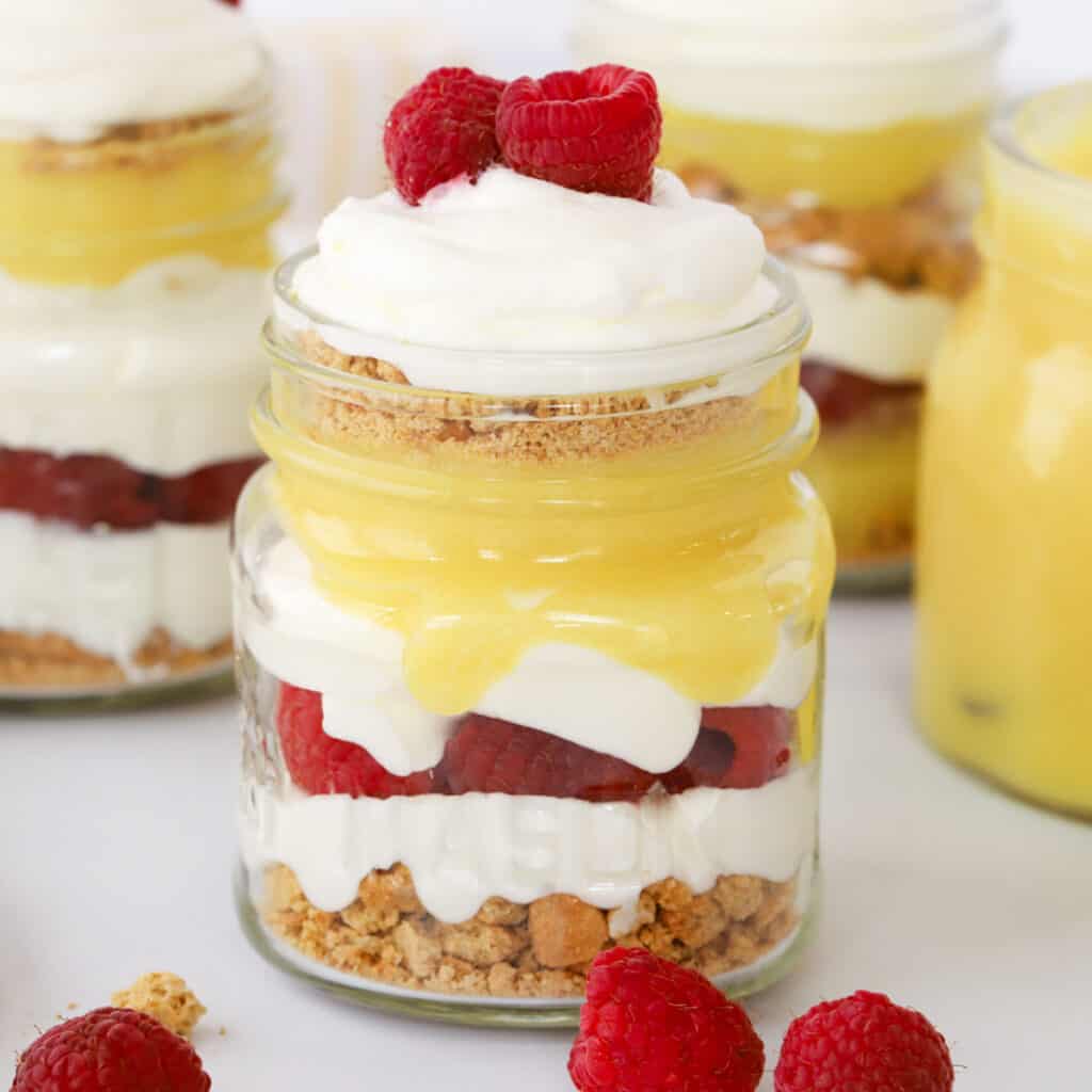 A mason jar with a lemon and raspberry parfait made with lemon curd, cream, crumble, and fresh raspberries. easy easter parfait for easter dessert.