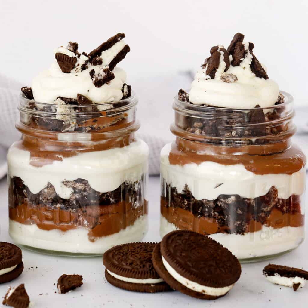 Oreo Parfaits in glass jars topped with whipped cream and Oreos.