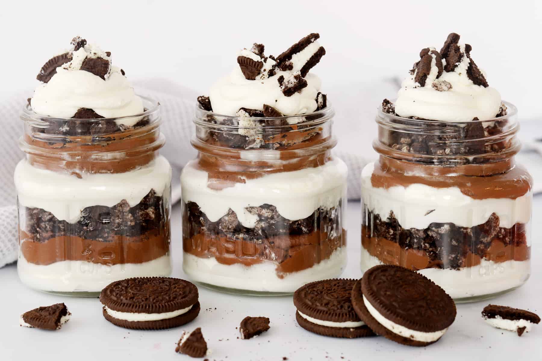 Three individual glass jars full of chocolate and oreo parfaits on a table.