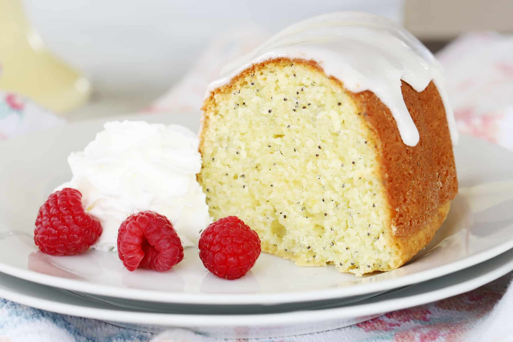 A slice of lemon poppy seed bundt cake on a white plate with whipped cream and berries.