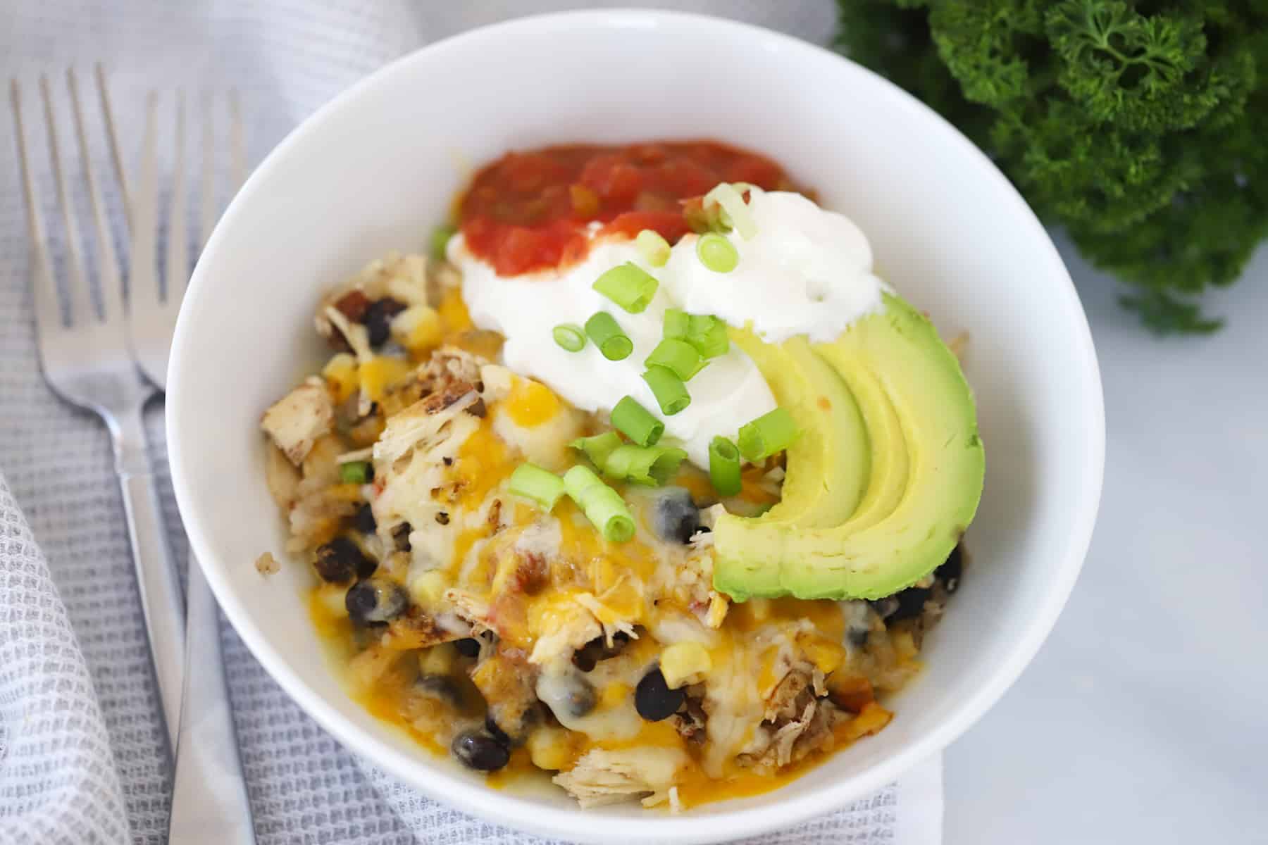 A burrito bowl filled with chicken, beans, rice and cheese, topped with sour cream, salsa, avocado and onions.