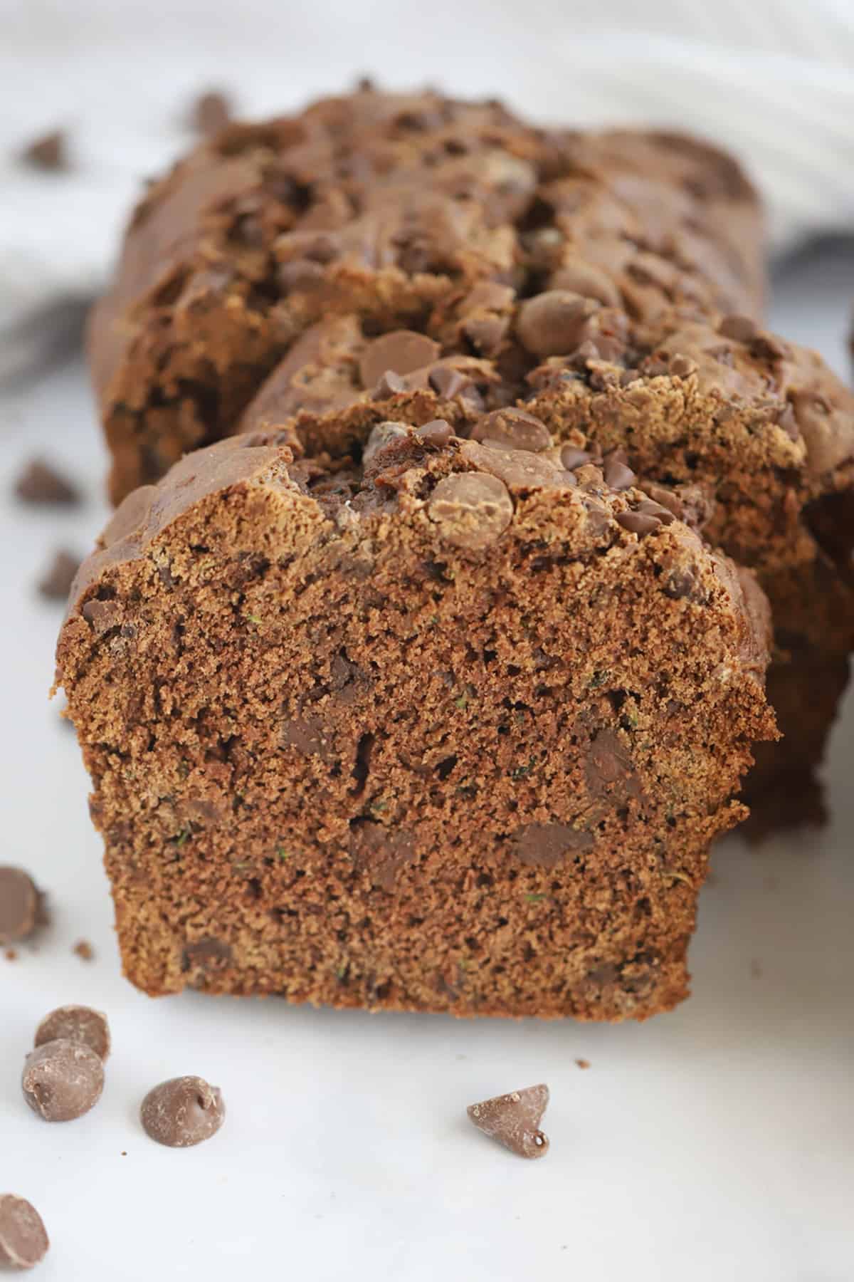 Slices of a loaf of chocolate zucchini bread on a table surrounded by chocolate chips.
