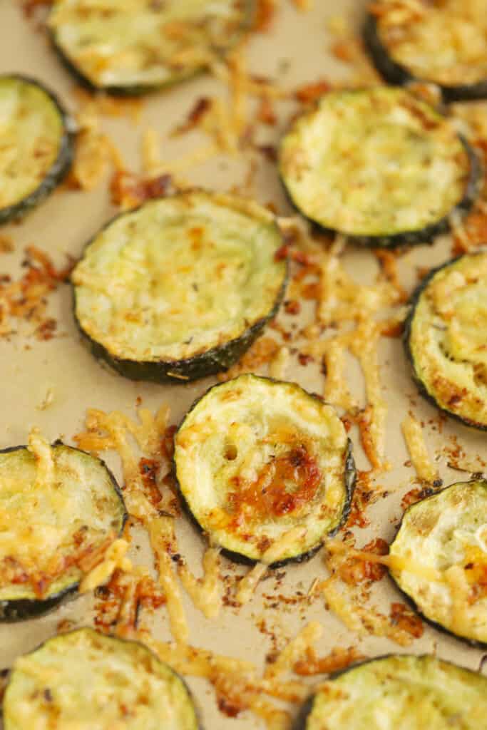 Baked parmesan zucchini on a baking sheet with golden brown cheese.