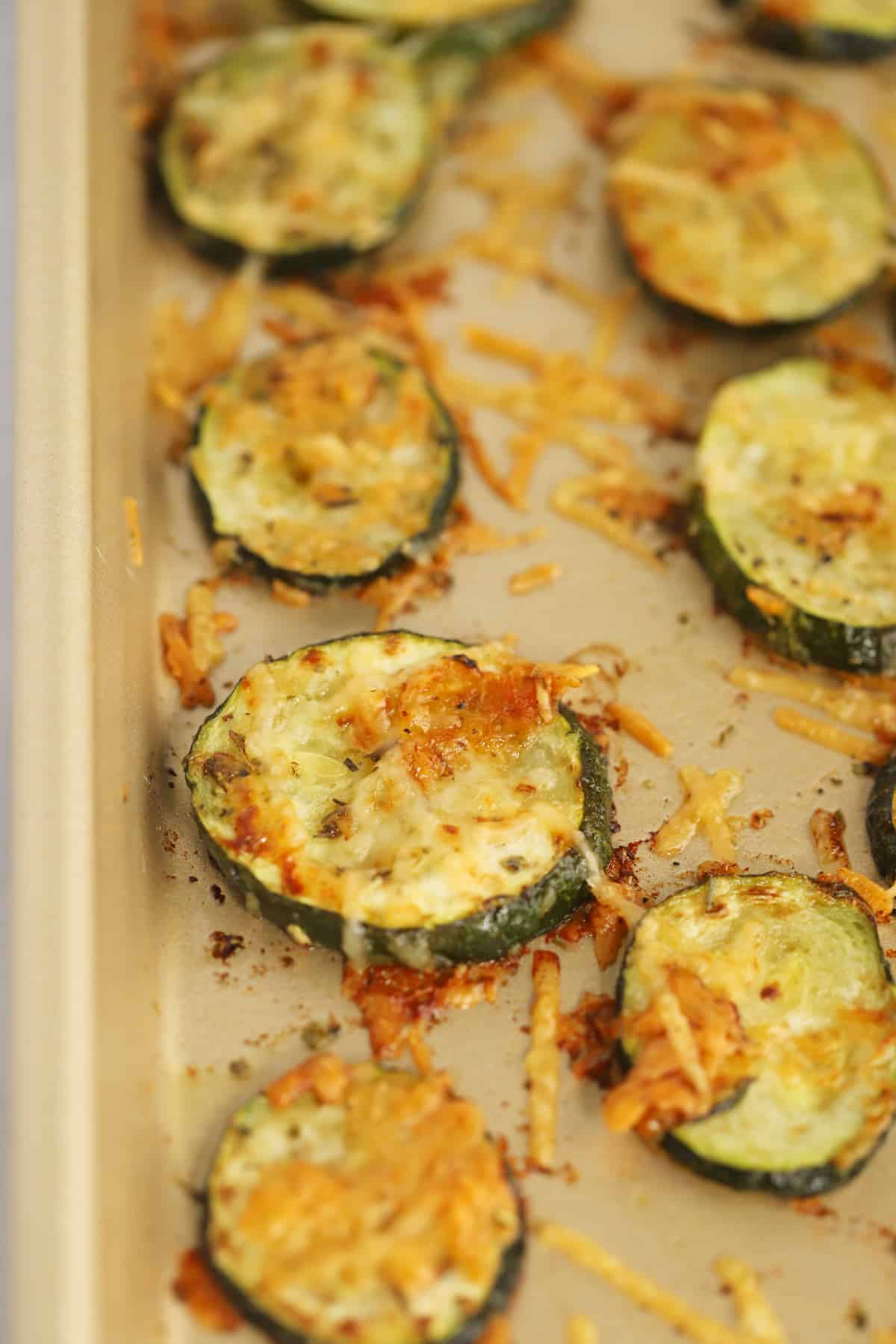 Sliced zucchini baked on a sheet tray covered with crispy Parmesan cheese.