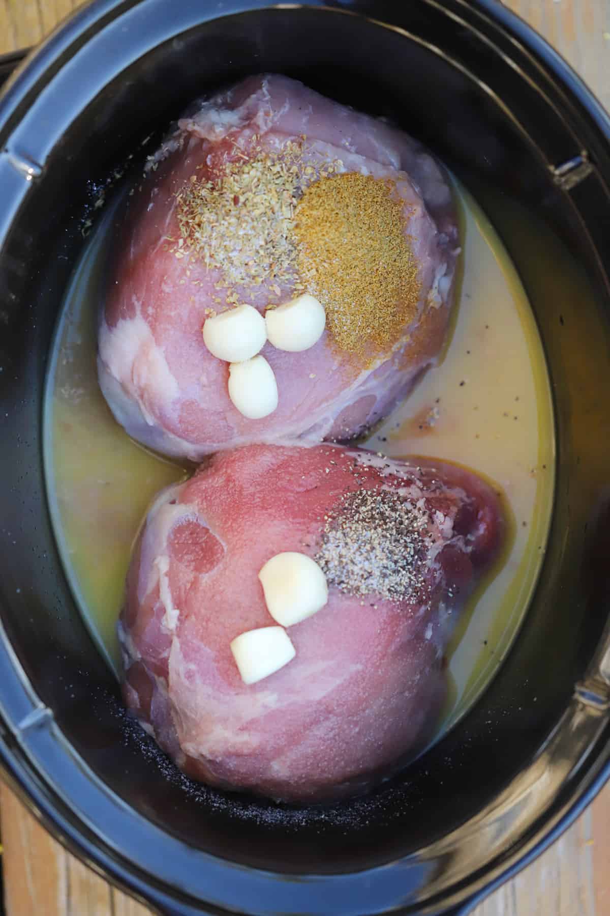 Raw pork in a slow cooker along with garlic, spices and broth.