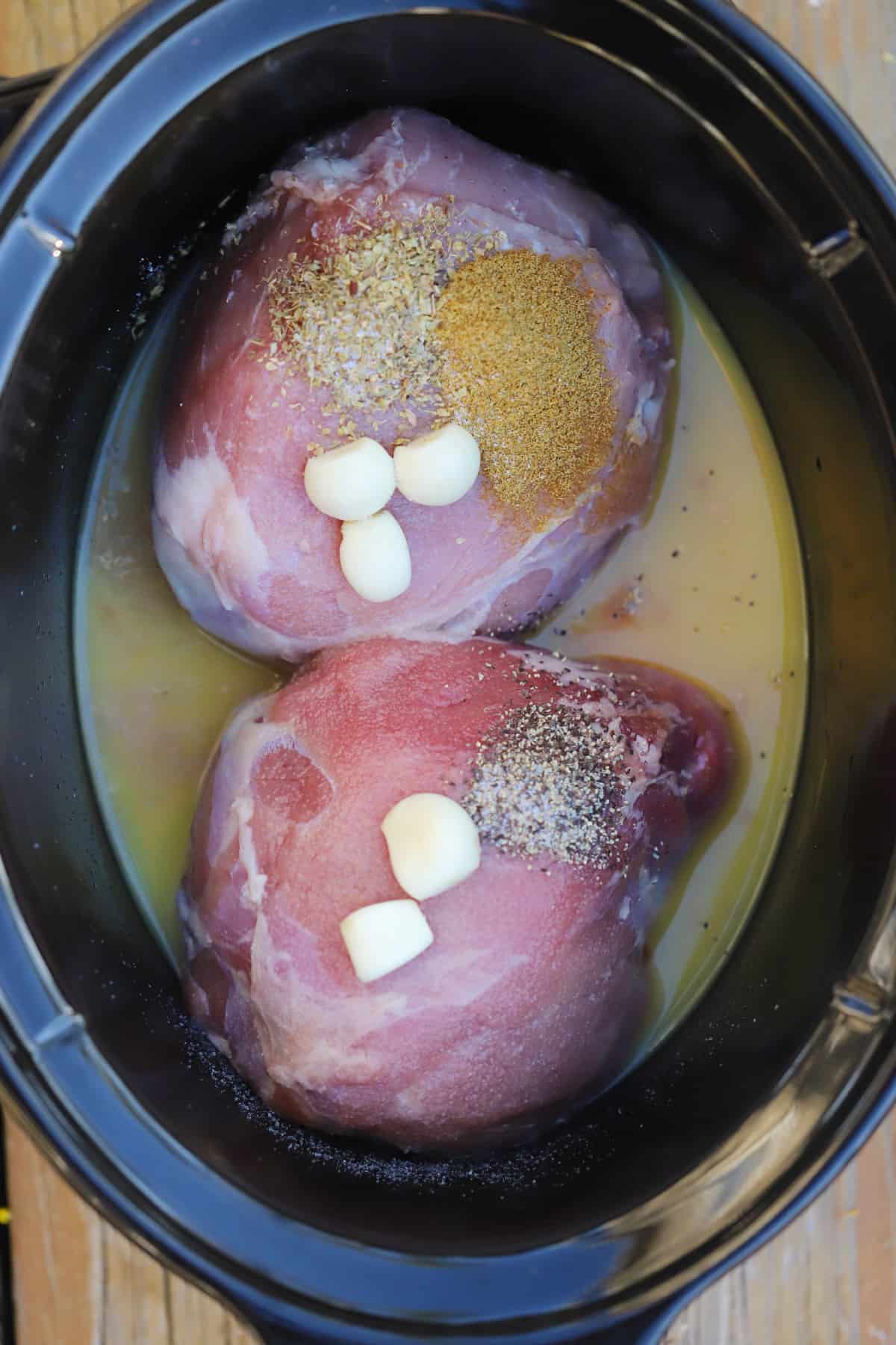 Pork roast in a slow cooker along with garlic, broth and spices.