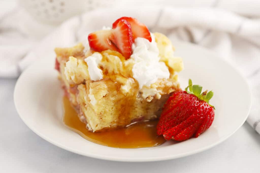 recipe for baked strawberry french toast on a plate topped with whipped cream and strawberries.