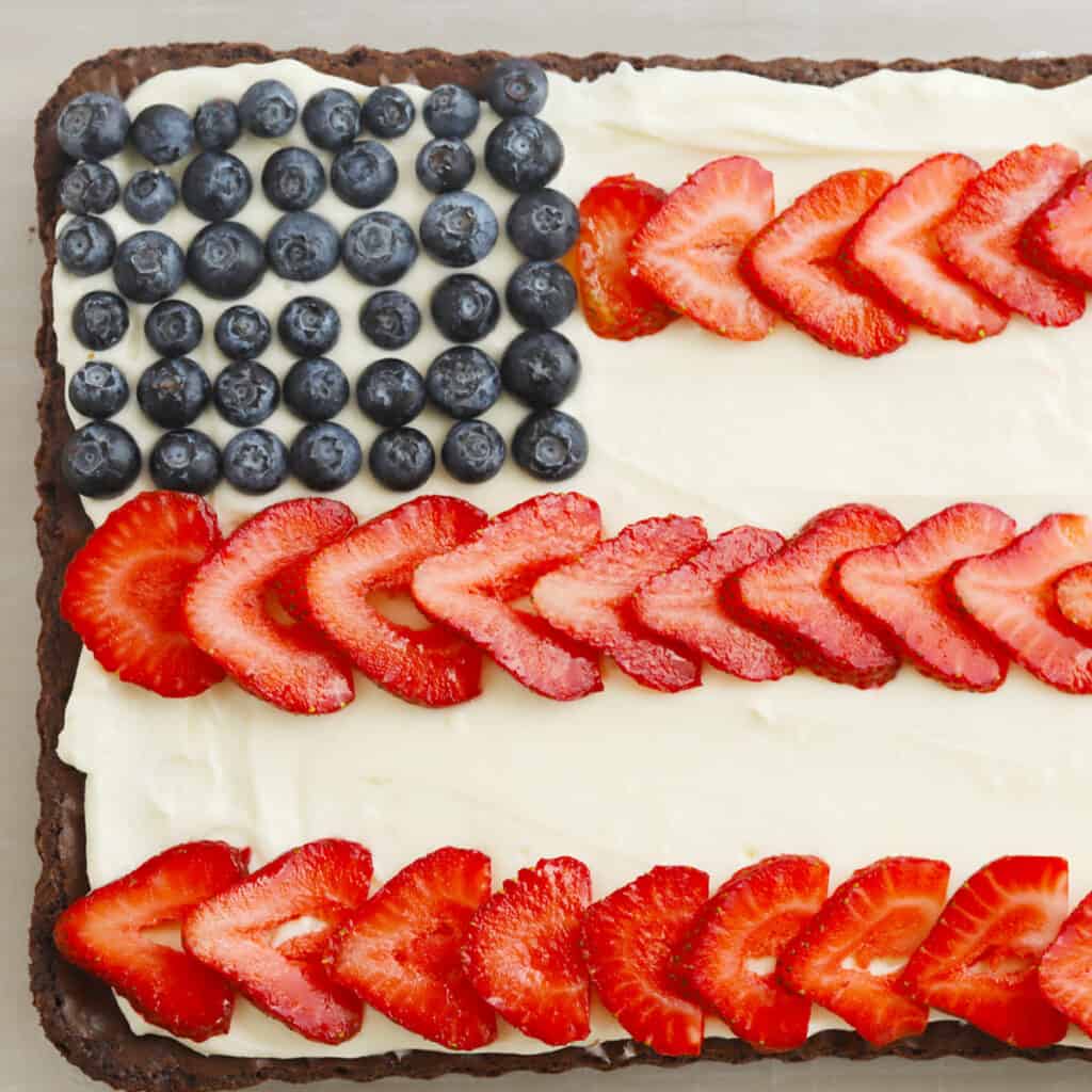 A sheet of brownies covered with cream cheese frosting and decorated with blueberries and sliced strawberries to look like the American flag.