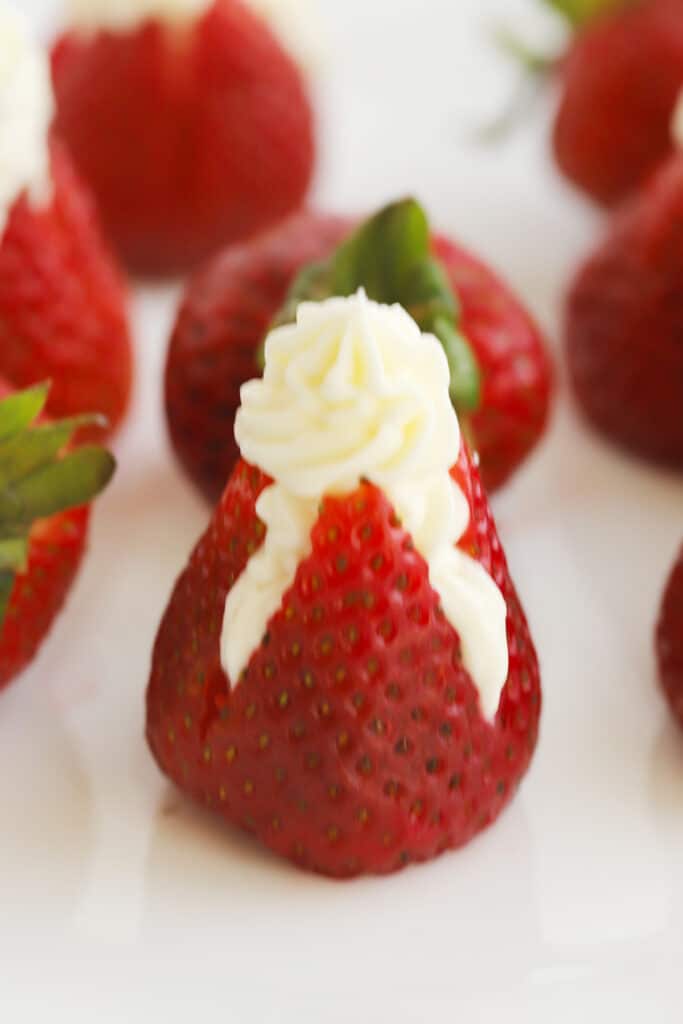 cheesecake filled strawberries on a white platter, ready to be served, strawberry stuffed cheesecake, cheesecake filling for strawberries. strawberry filled cheesecake.  