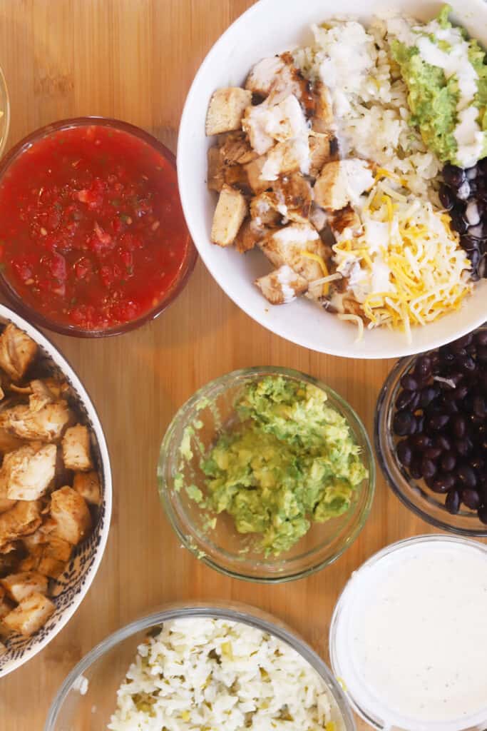 A chicken burrito bowl on a table with small ramekins of toppings.