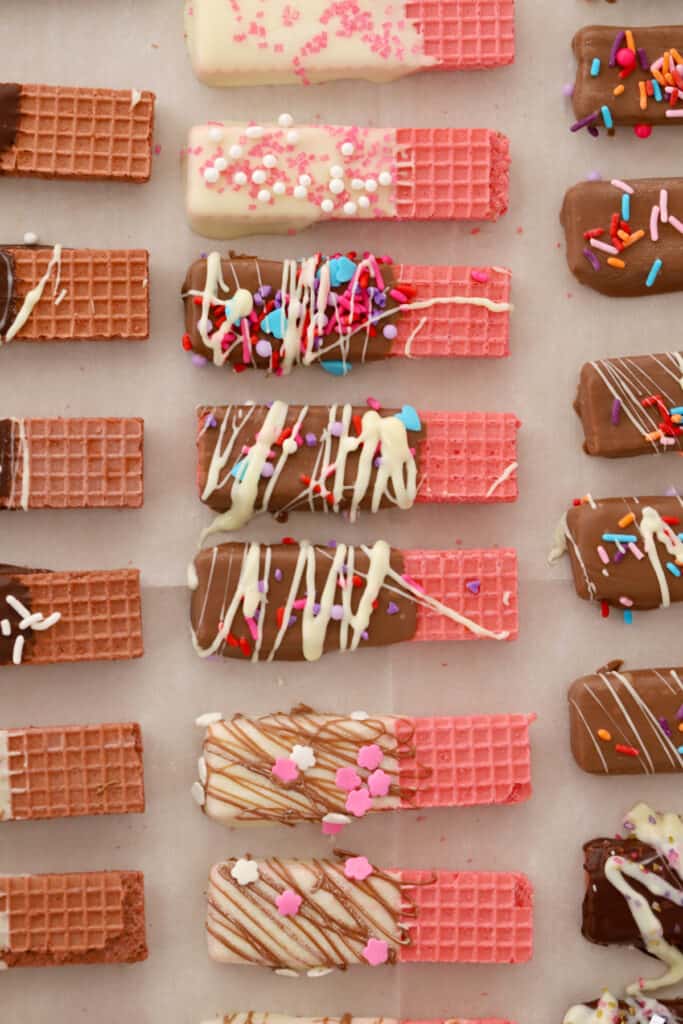 Chocolate dipped wafer cookies lined up on a sheet tray and decorated with different types of sprinkles and chocolate drizzles. Cookies wafer.