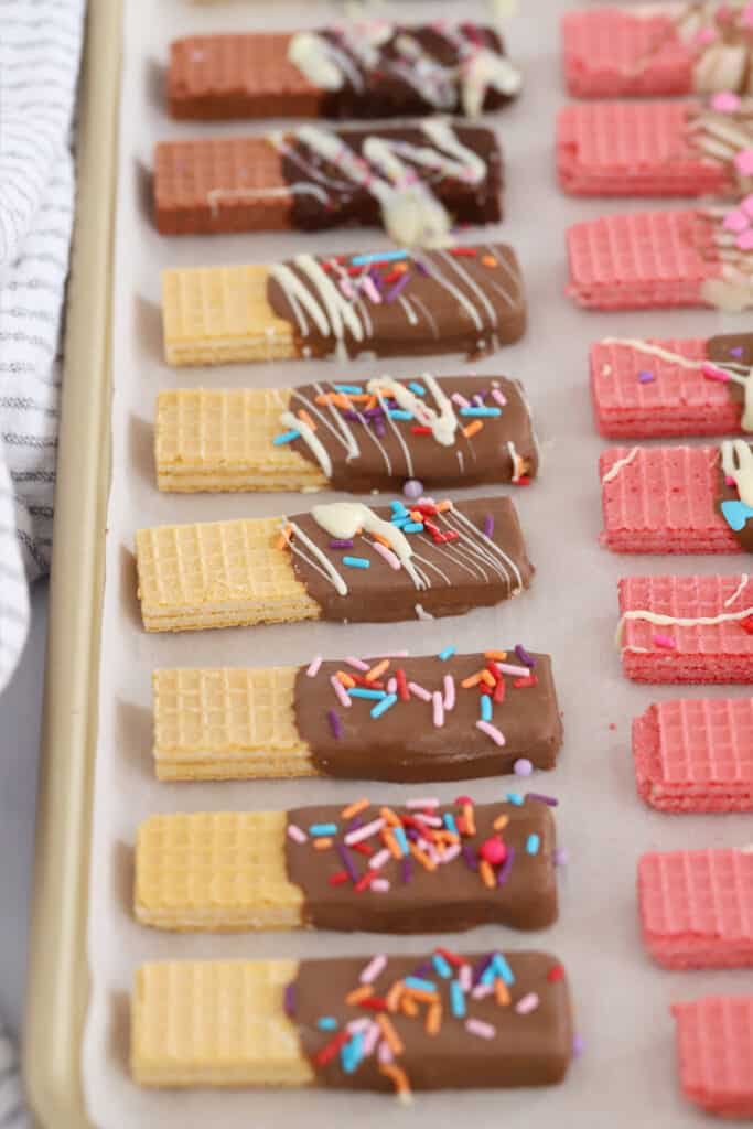 A sheet tray filled with wafer cookies dipped in chocolate and covered with sprinkles.