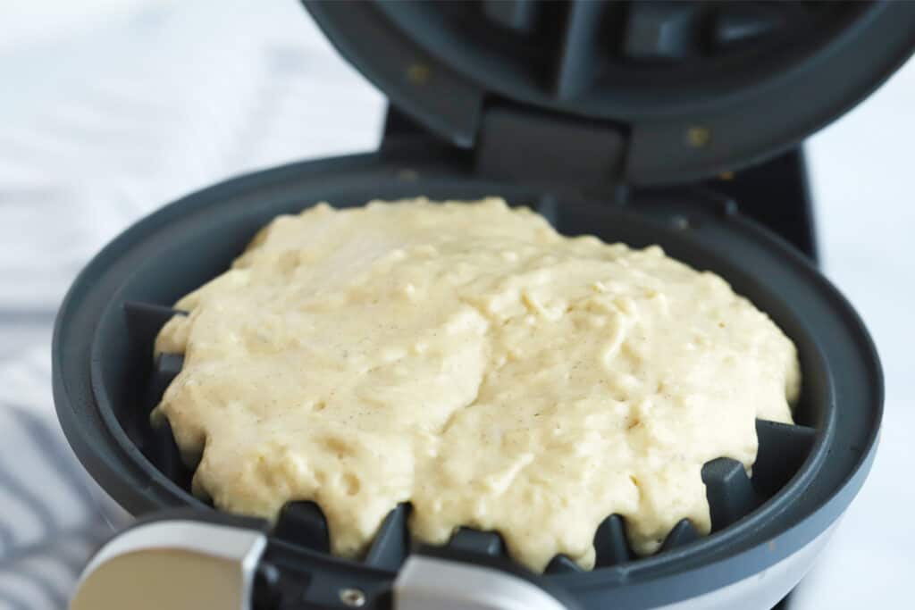 A waffle iron opened with batter in the center.