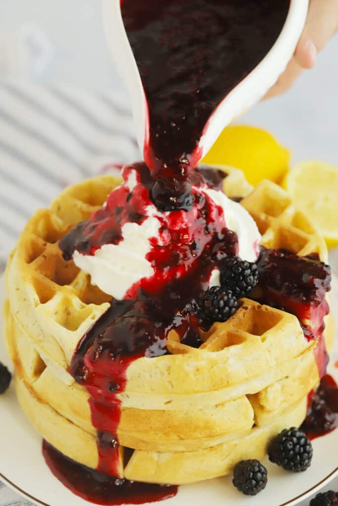 A small pitcher pouring blackberry syrup over waffles on a plate. blackberry breakfast recipes. 