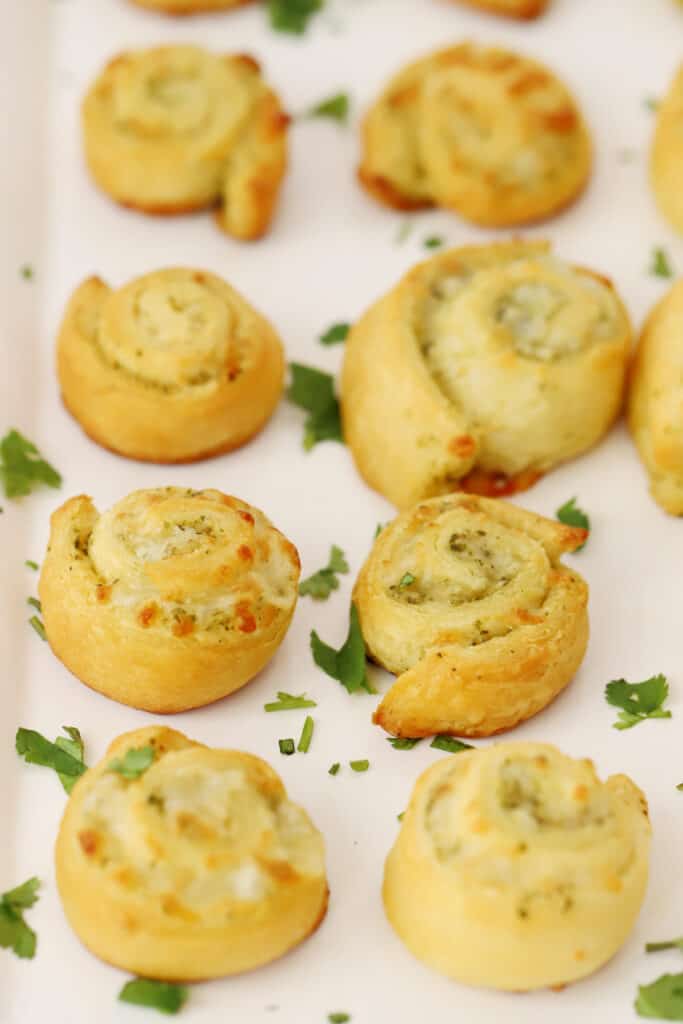 Pesto pinwheels garnished with fresh parsley on a serving plate.