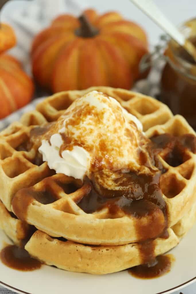 Waffles on a plate topped with syrup and whipped cream. pumpkin spice homemade syrup.
