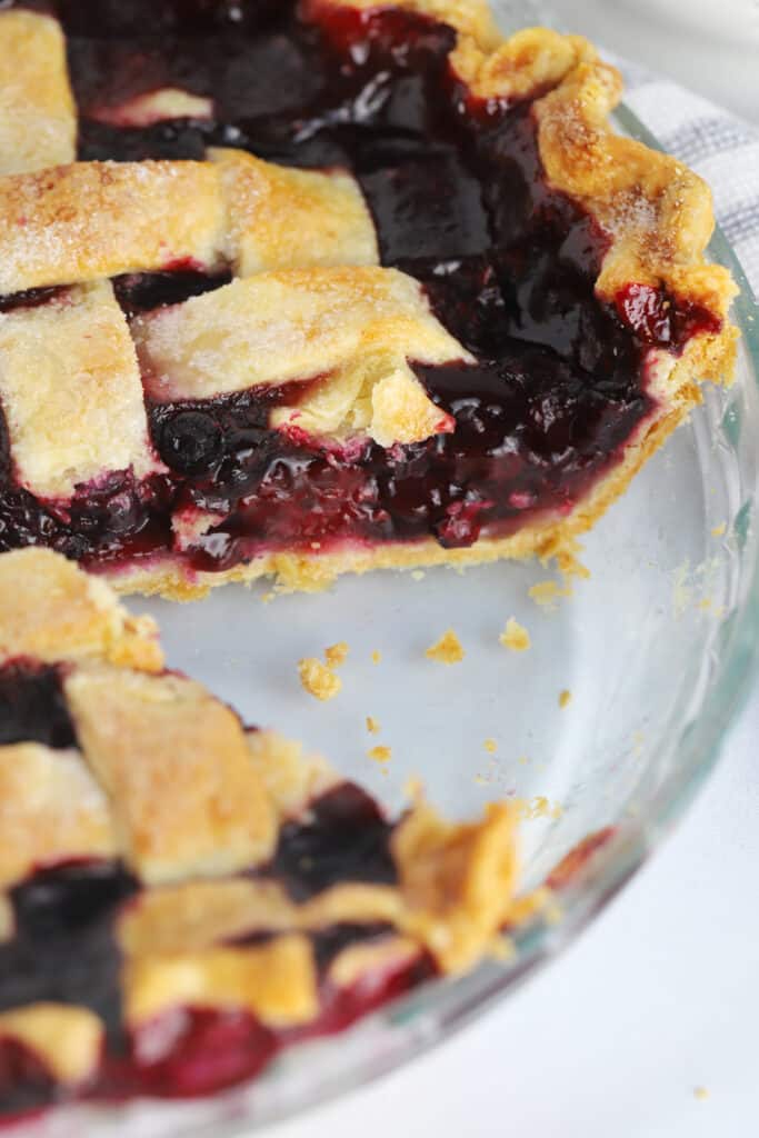 A glass pie plate with a Razzleberry pie that has a slice removed. Razzleberry pie recipes.