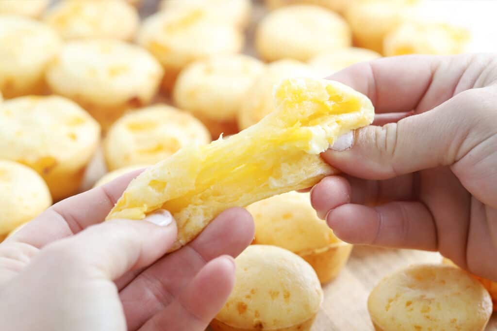 Hands pulling apart a Brazilian cheese puff.