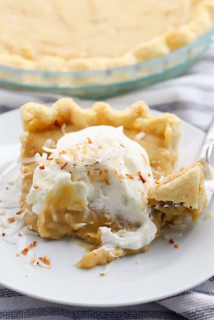 A slice of coconut butterscotch cream pie topped with whipped cream on a pie plate. butterscotch pie recipes. 
