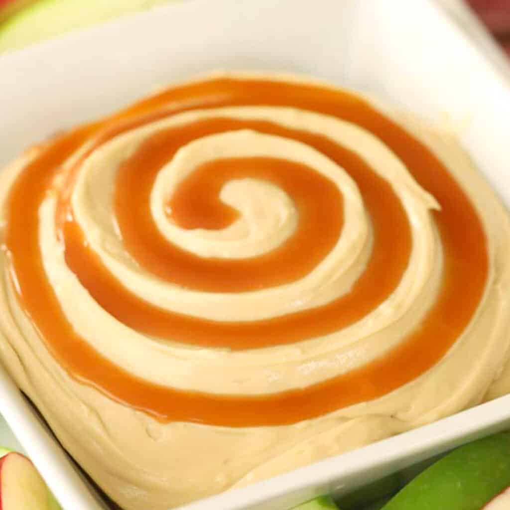 A serving bowl full of cream cheese dip with a swirl of caramel.